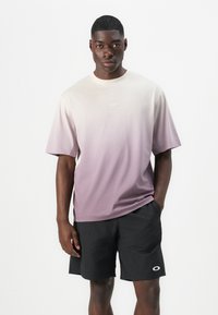 Kurzarm-T-Shirt in einem Farbverlauf von hellem Creme zu Lavendel, aus Baumwolle gefertigt, mit einem runden Logo auf der Brust.