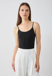 Svart ärmlös topp med tunna axelremmar, med en figurnära design. Matchad med högmidjade vita byxor, slät textur och skräddarsydd passform.