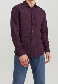 Rödbrun och marinblå randig knäppt skjorta med långa ärmar, krage och svarta knappar, kombinerad med blå jeans.