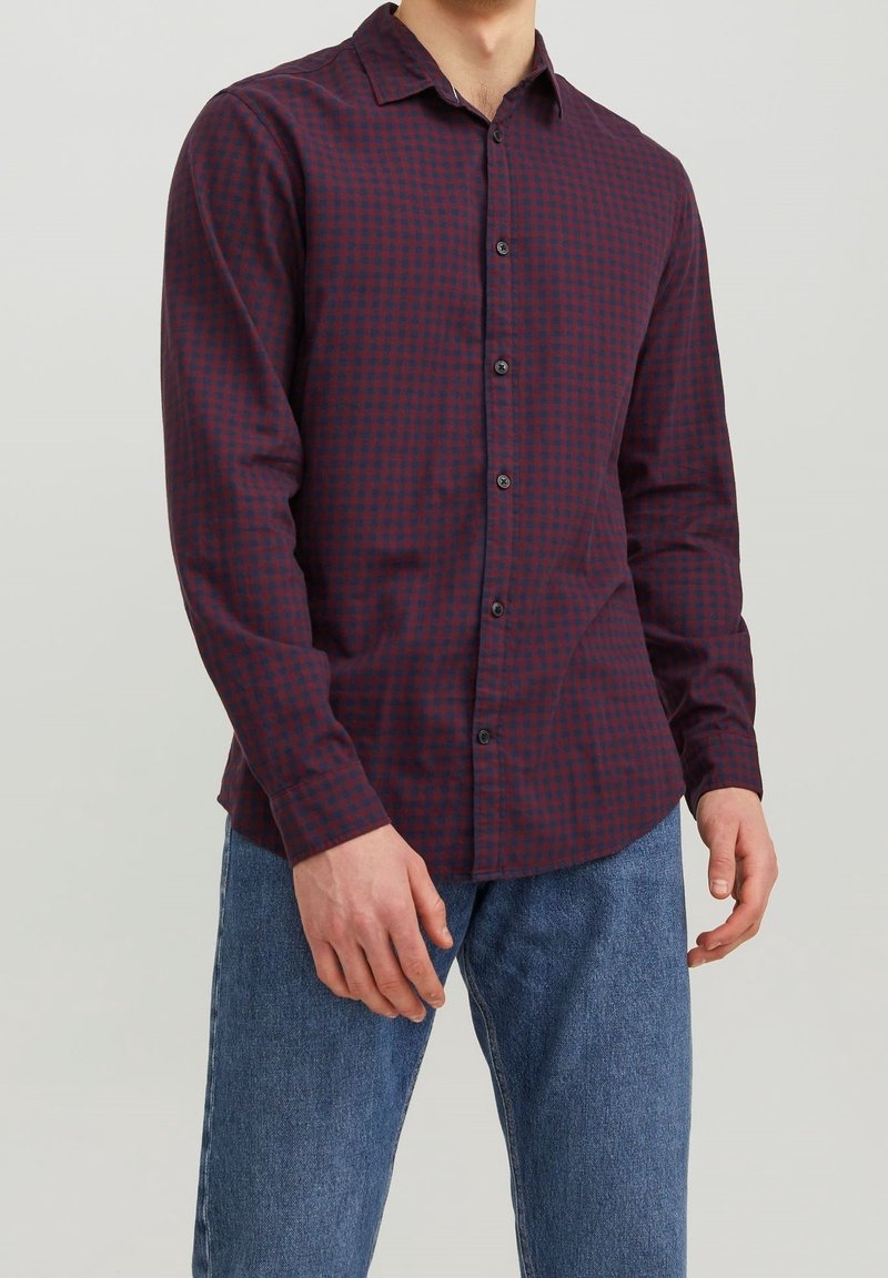 Rödbrun och marinblå randig knäppt skjorta med långa ärmar, krage och svarta knappar, kombinerad med blå jeans.