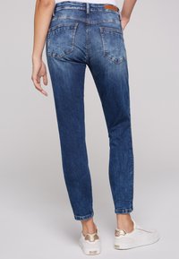 Jeans de denim azul con un corte relajado, que presentan una textura desvaída, cinco bolsillos y un dobladillo enrollado, combinados con zapatillas blancas.