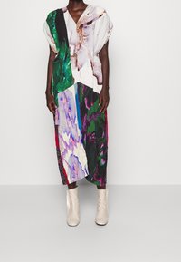 Robe midi plissée avec un décolleté en V, présentant un design abstrait multicolore. Portée avec des bottines beige clair, créant un look contrasté.