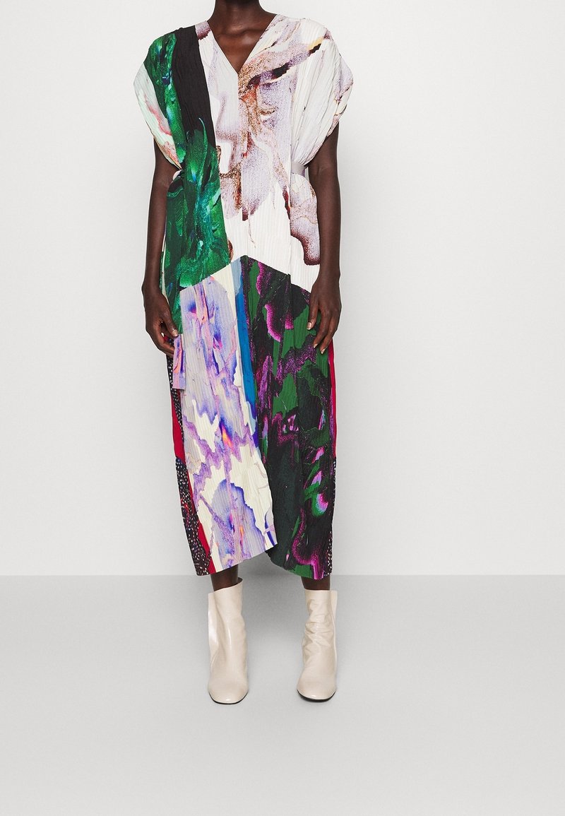 Robe midi plissée avec un décolleté en V, présentant un design abstrait multicolore. Portée avec des bottines beige clair, créant un look contrasté.