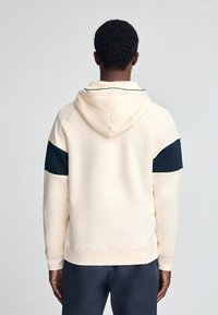 Crème hoodie met een marineblauwe streep op de mouwen. Voorzien van een trekkoord capuchon en geribbelde manchetten, gemaakt van zachte stof voor comfort.