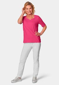 Kurzärmlige rosa Bluse mit rundem Ausschnitt, kombiniert mit weißen Hosen und hellen Turnschuhen. Glattes Material mit lässiger Passform.