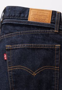 Mörkblå jeans i denim med orange sömmar, med en brun läderlapp märkt "Levi Strauss & Co." och en liten röd logotyp på sömmen.