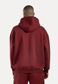 Sudadera con capucha color burdeos hecha de una tela suave, con un corte relajado, puños acanalados y un dobladillo con banda; detalles de costura visibles.