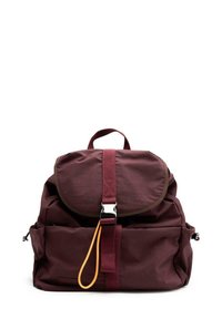 Zaino in tessuto bordeaux con flap arrotondato, spallacci regolabili, una fibbia argentata e un tirante arancione a contrasto. Presenta tasche frontali.