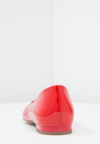 Czerwona balerina z lakierowanej skóry z zaokrąglonym noskiem i niewielkim obcasem, charakteryzująca się gładką, błyszczącą powierzchnią oraz kontrastującą beżową podeszwą.