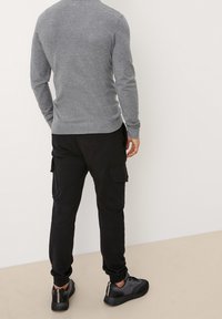 Pull gris à manches longues, cintré, avec ourlet et poignets côtelés. Pantalon de survêtement cargo noir avec poches latérales. Baskets noires texturées avec accents.