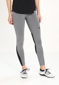 Leggings gris avec des panneaux latéraux noirs, présentant une texture lisse et une coupe ajustée. Assortis avec un haut noir et des chaussures de sport blanches.