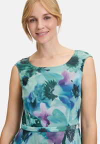 Blumenkleid mit türkisfarbenem und lila Druck, ärmelloses Design mit rundem Ausschnitt und einer taillierten Silhouette, die an der Taille betont wird.