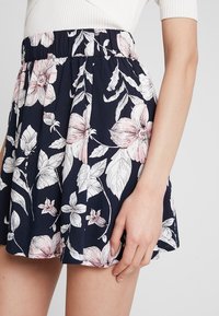 Blommig kjol med en marinblå bakgrund och stora rosa och vita blommor, elastisk midja och en utsvängd design med en mjuk textur.