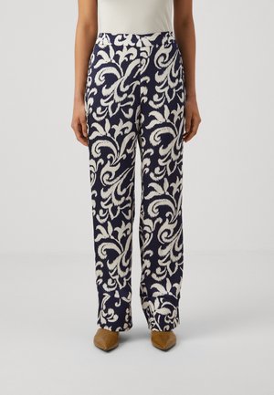 Pantalon à motifs navy avec un design floral blanc, doté d'une taille haute et d'une coupe évasée. Le tissu semble lisse avec un léger brillant.