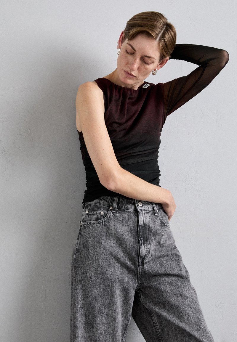 Débardeur en dégradé noir et bordeaux avec un design sans manches, associé à un jean en denim gris taille haute, au fit loose et à la texture délavée.
