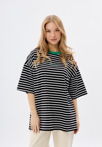 Zwart-wit gestreepte oversized t-shirt met een groene ribbelkraag en een klein groen logo. Korte mouwen en van zacht katoen.