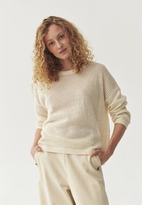 Maglione leggero in maglia con un motivo a trama aperta, scollo rotondo e maniche lunghe, abbinato a pantaloni beige.
