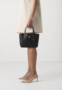 Zwarte handtas met textuur en twee handvatten, met een logo-accent en een gestructureerde rechthoekige vorm. Geplaatst tegen een neutrale achtergrond.