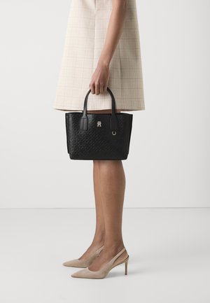 Bolso de mano negro texturizado con dos asas, que presenta un acento de logo y una forma rectangular estructurada. Colocado sobre un fondo neutro.