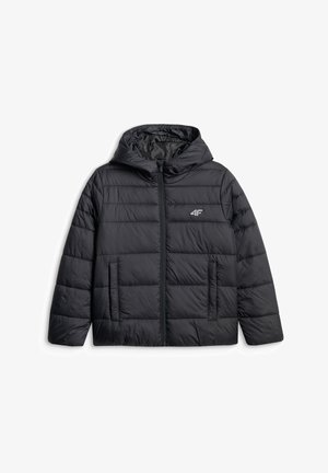 Garçon portant une veste à capuche noire, un bonnet vert olive, un pantalon cargo gris et des baskets blanches, debout les mains dans les poches regardant sur le côté.