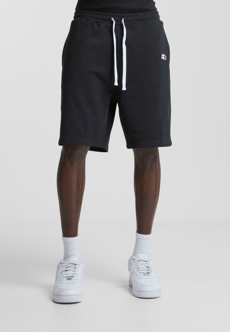 Pantalones cortos deportivos negros de algodón con cintura ajustable. Presenta un pequeño logo en la parte delantera y un ajuste relajado que termina por encima de la rodilla.