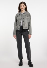 Grijze denimjas met rafelrand en manchetten, voorzien van een knoopsluiting en twee borstzakken, gecombineerd met zwarte high-waisted jeans en zwarte laarzen.