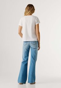 Λευκό βαμβακερό t-shirt με κοντά μανίκια, συνδυασμένο με ανοιχτό μπλε τζιν καμπάνα με τσέπες στην πλάτη και ακατέργαστη λεπτομέρεια στο τελείωμα.