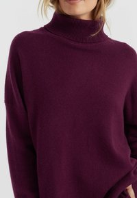 Paarse oversized coltrui gemaakt van zachte gebreide stof. Heeft een geribbelde kraag en verlaagde schouders, wat zorgt voor een ontspannen silhouet.