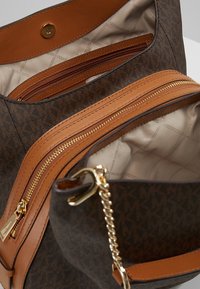 Sac à main marron avec monogramme, accents en cuir beige et quincaillerie dorée. Comprend deux compartiments zippés et un intérieur doublé.