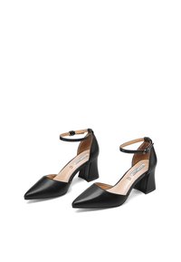 Scarpe nere in pelle con tacco alto, punta affilata, cinturini alla caviglia e tacco a blocco. Texture liscia, design minimalista e senza motivi visibili.