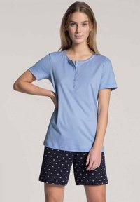 Lichtblauw kort mouwtopje met een ronde hals en knoopsluiting, gecombineerd met marineblauwe shorts met een subtiel wit patroon.