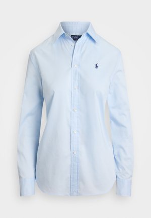 Camisa azul claro de botones, hecha de algodón, con mangas largas, un collar clásico y un pequeño logo azul marino en el pecho. Textura suave.