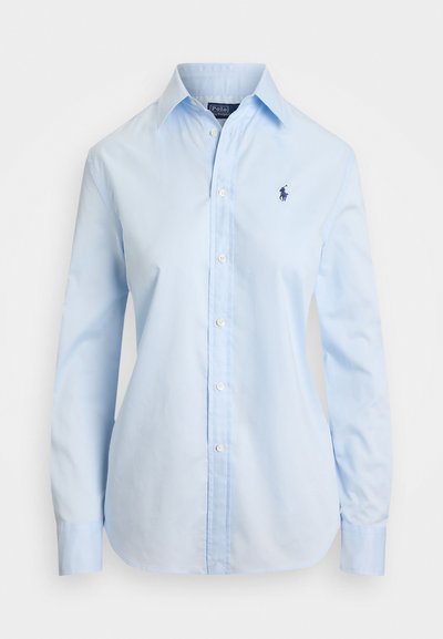 Gaiši zils krekls ar garām piedurknēm, izgatavots no kokvilnas, ar klasisku apkakli un mazu tumši zilas krāsas logo uz krūts. Gluda auduma tekstūra.