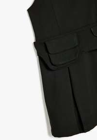 Vêtement sans manches noir, doté de deux poches avant, au design structuré et à la finition lisse et texturée. Adapté pour être superposé.