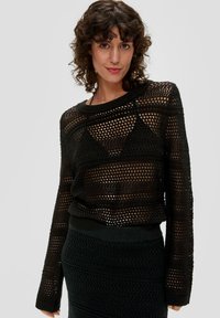 Czarny sweter o otwartym splocie z długimi rękawami, z teksturowanym paskowanym wzorem; noszony na dopasowanej czarnej spódnicy.