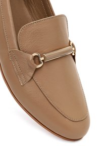 Beige leather loafer with a rounded toe, featuring a gold-tone bar and linking hardware accents. Smooth texture and stitching visible.