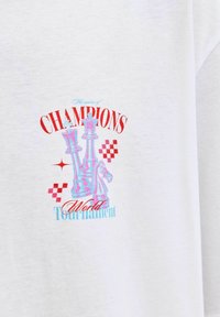 Balta kokvilnas T-kreklu ar krāsainu šaha figūru grafiku, uz kuras ir teksts "ČEMPIONU spēle Pasaules turnīrs" sarkanā un zilā krāsā.