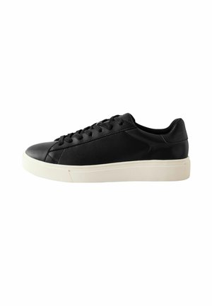 Baskets en cuir noir avec un bout arrondi, des accents texturés, des lacets plats et une semelle en caoutchouc blanche. Vue de côté montrant un design épuré.