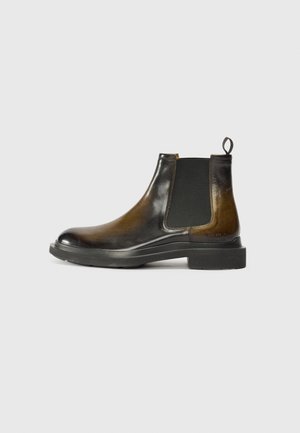 Botín Chelsea de cuero marrón y negro con paneles laterales elásticos, puntera redonda y un tacón texturizado. Cuenta con una lengüeta y una suela de goma resistente.
