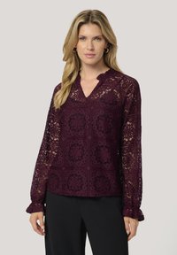 Top in pizzo borgogna con maniche lunghe, caratterizzato da un collo a sbuffo e da un motivo floreale, con dettagli testurizzati e complessi tagli, e polsini arricciati.