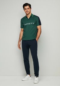 Zelená polokošeľa s námorníckymi rukávmi a limetkovými akcentmi, s logom "HACKETT" v šedej farbe. Spárovaná s námorníckymi nohavicami a bielymi teniskami.
