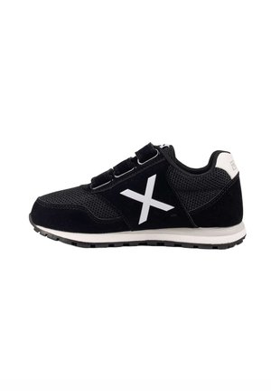 Zapatilla negra con suela blanca, gran "X" blanco en el lateral, tres tiras de velcro negras y detalles de tela de malla.
