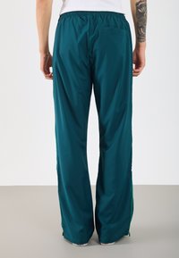 Türkise, locker sitzende Sweatpants mit elastischem Bund und seitlichen Reißverschlusstaschen, aus einem glatten, leichten Stoff.