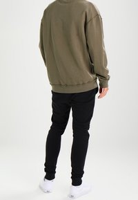 Sudadera verde oliva con un corte relajado, cuello redondo y dobladillo acanalado, combinada con pantalones pantalones negros ajustados y zapatillas blancas.