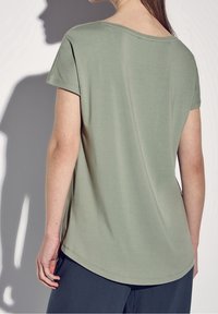 Grön bomullströja med lös passform, korta ärmar, rundad halsringning och en något krökt nederkant. Slät textur, minimal detaljering.