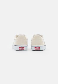 Vans Sneakers aus beigem Wildleder und weißem Canvas mit einem Low-Top-Design, das einen schwarzen Streifen und ein rotes Logo auf der Ferse zeigt.