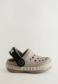 Jasno brązowe Crocs z otworami wentylacyjnymi i czarnym regulowanym paskiem na pięcie, z nadrukiem "BAKER by TED BAKER" z boku.