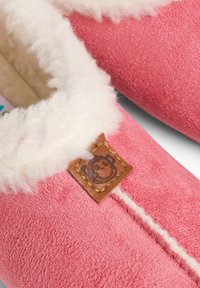 Chaussons roses en tissu doux avec une doublure intérieure en fourrure blanche. Comprend un patch en cuir marron avec un design de singe et des coutures blanches.