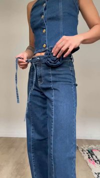 Persona con top sin mangas de mezclilla y jeans de cintura alta, ajustándose un cinturón de mezclilla a juego con una hebilla en forma de flor.