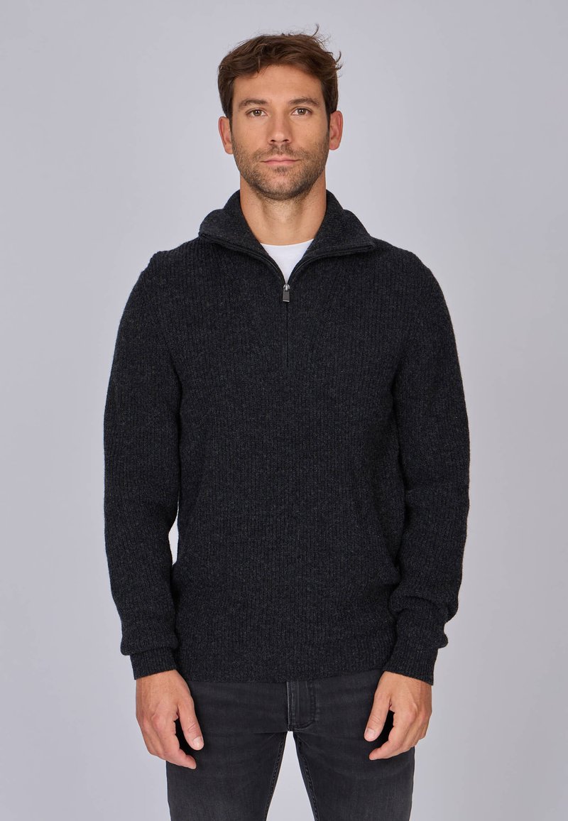 Pull en maille gris foncé avec un col montant et une fermeture éclair partielle. Il présente une texture côtelée et des manches longues. Associé à un jean foncé.